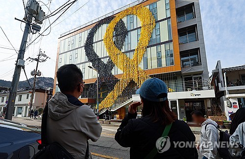(서울=연합뉴스) 서대연 기자 = 세월호 참사 10주기를 보름여 앞둔 31일 오후 시민들이 서울 종로구 참여연대 건물 외벽에 설치된 대형 추모 리본을 바라보고 있다. 2024.3.31 dwise@yna.co.kr