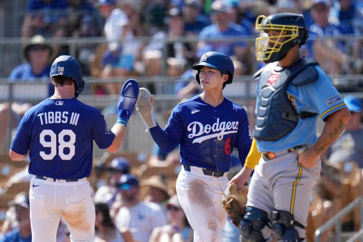 Los Angeles Dodgers' Hyeseong Kim (6), of South Korea, and James Tibbs III (98) celebrate their runs scored as Milwaukee Brewers catcher Gary Sanchez pauses near home plate during the third inning of a spring training baseball game, Monday, March 16, 2026, in Phoenix. (AP Photo/Ross D. Franklin)