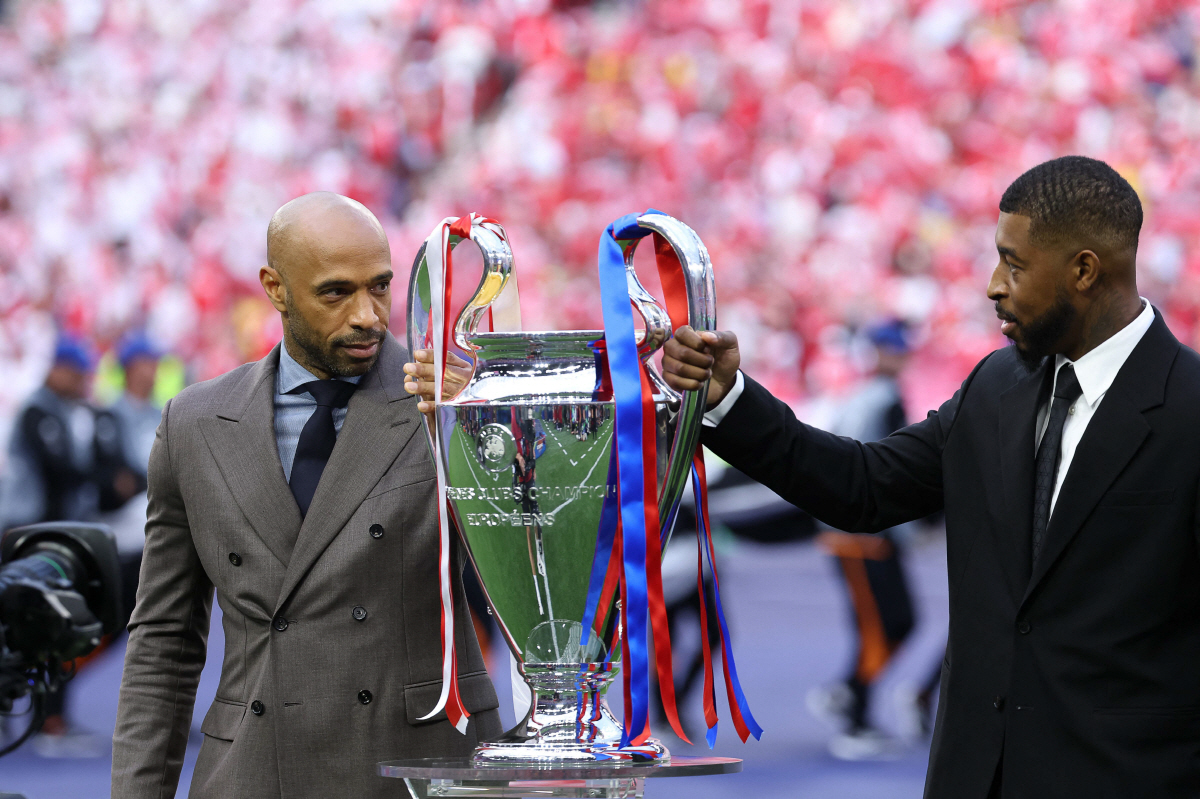 French former Arsenal FC player Thierry Henry (L) and French former Paris Saint-Germain (PSG) Presnel Kimpembe present the Champions League trophy before the start of the UEFA Champions League final football match between Paris Saint-Germain (PSG) and Arsenal FC at the Puskas Arena in Budapest on May 30, 2026. (Photo by FRANCK FIFE / AFP)