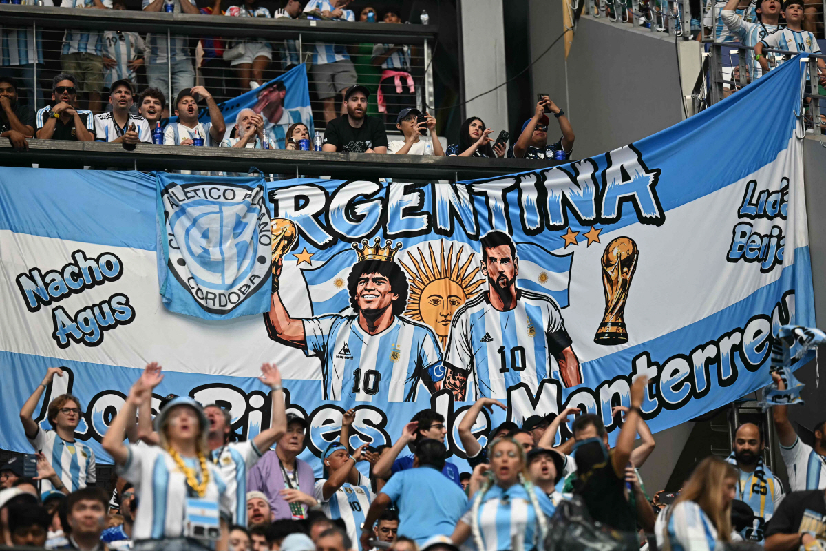 Argentina supporters cheer in front of a banner depicting late Argentine football player Diego Maradona and Argentina's forward #10 Lionel Messi during the 2026 World Cup Group J football match between Argentina and Austria at the Dallas Stadium in Arlington on June 22, 2026. (Photo by Paul ELLIS / AFP)