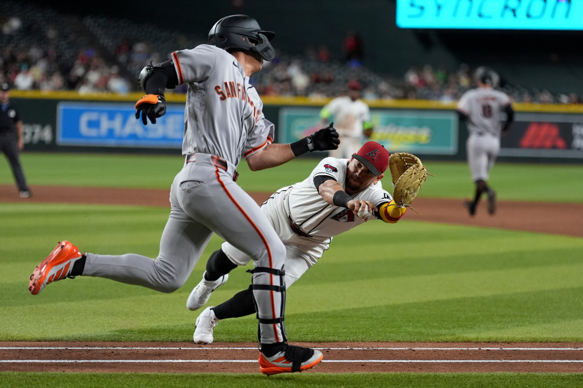 Arizona Diamondbacks first baseman Ildemaro Vargas, right, dives to tag San Francisco Giants' Jung Hoo Lee, left, who was ruled out of the baseline for the out during the ninth inning of a baseball game, Monday, June 29, 2026, in Phoenix. (AP Photo/Ross D. Franklin)