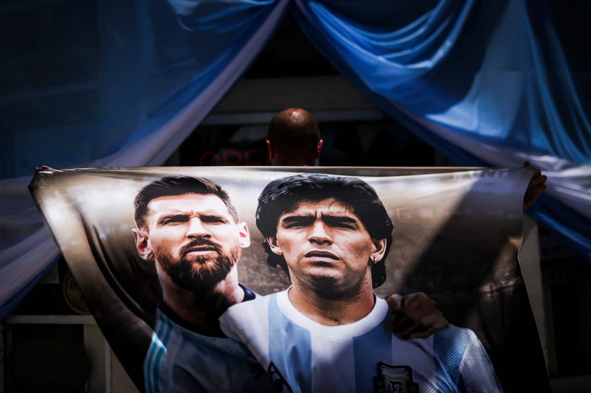 An Argentine fan, holding a flag that depicts Argentine football player Lionel Messi and football legend Diego Maradona, waits outside a restaurant to watch the 2026 FIFA World Cup group round of 16 match between Argentina and Egypt in Miami Beach, Miami on July 7, 2026. (Photo by PATRICIA DE MELO MOREIRA / AFP)